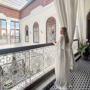 A woman in a white dress standing on a balcony with ornate railings and patterned tiles. - Riad Alassala Fes (Fes)