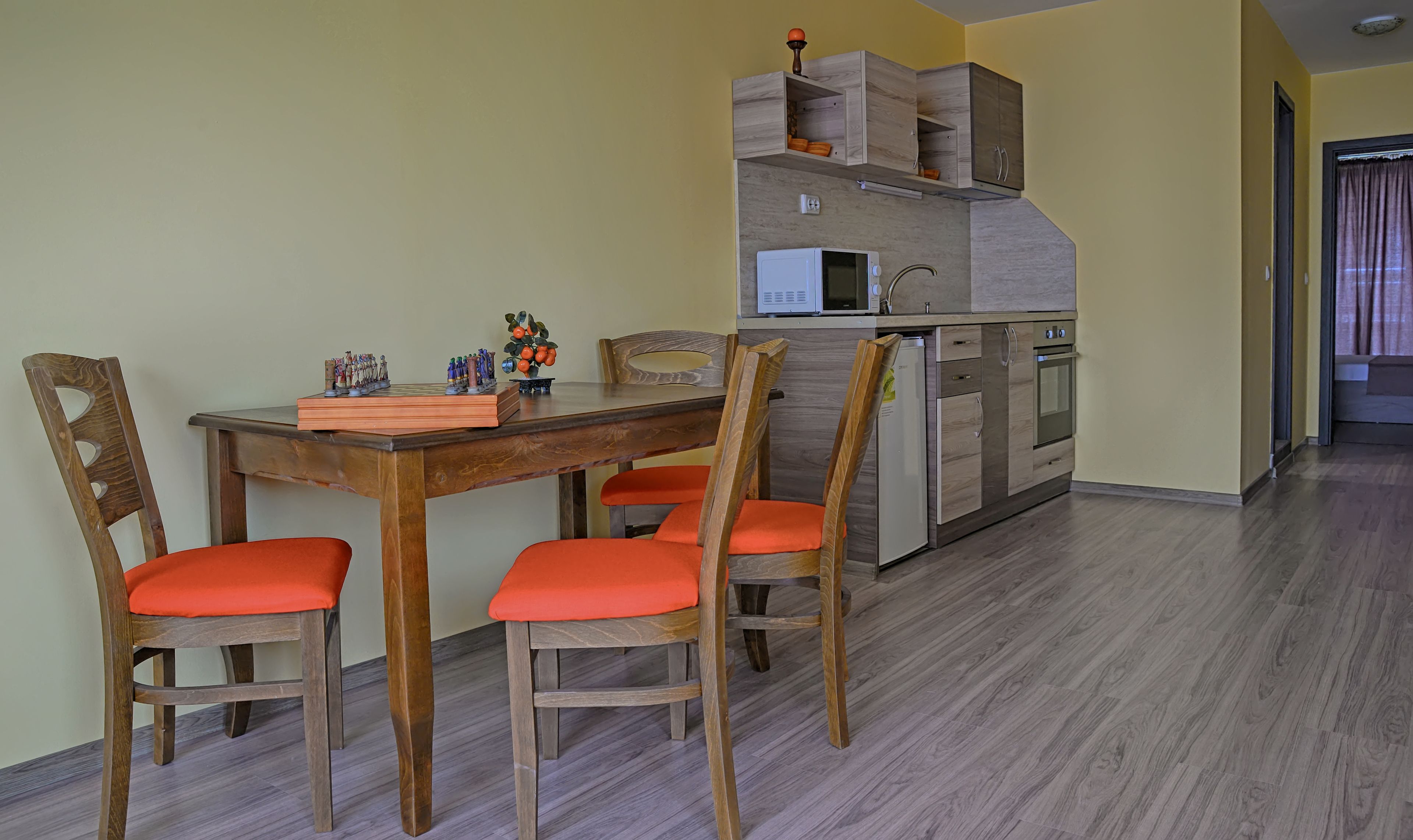 Un comedor con mesa y sillas de madera, una cocina con electrodomésticos integrados y una pared amarilla.