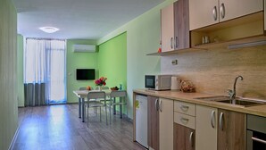 A modern kitchen with wooden cabinets, a microwave, and a sink. There is a dining area with chairs and a table, and a TV mounted on the wall. - Visito Apart House (Sofia)