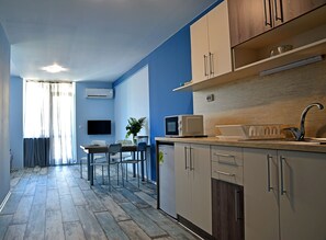 A modern kitchen with a microwave, sink, and cabinets. There is a dining area with chairs and a table. - Visito Apart House (Sofia)