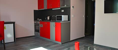 A modern kitchen with red and grey cabinets, a microwave, and a glass table with a red vase.