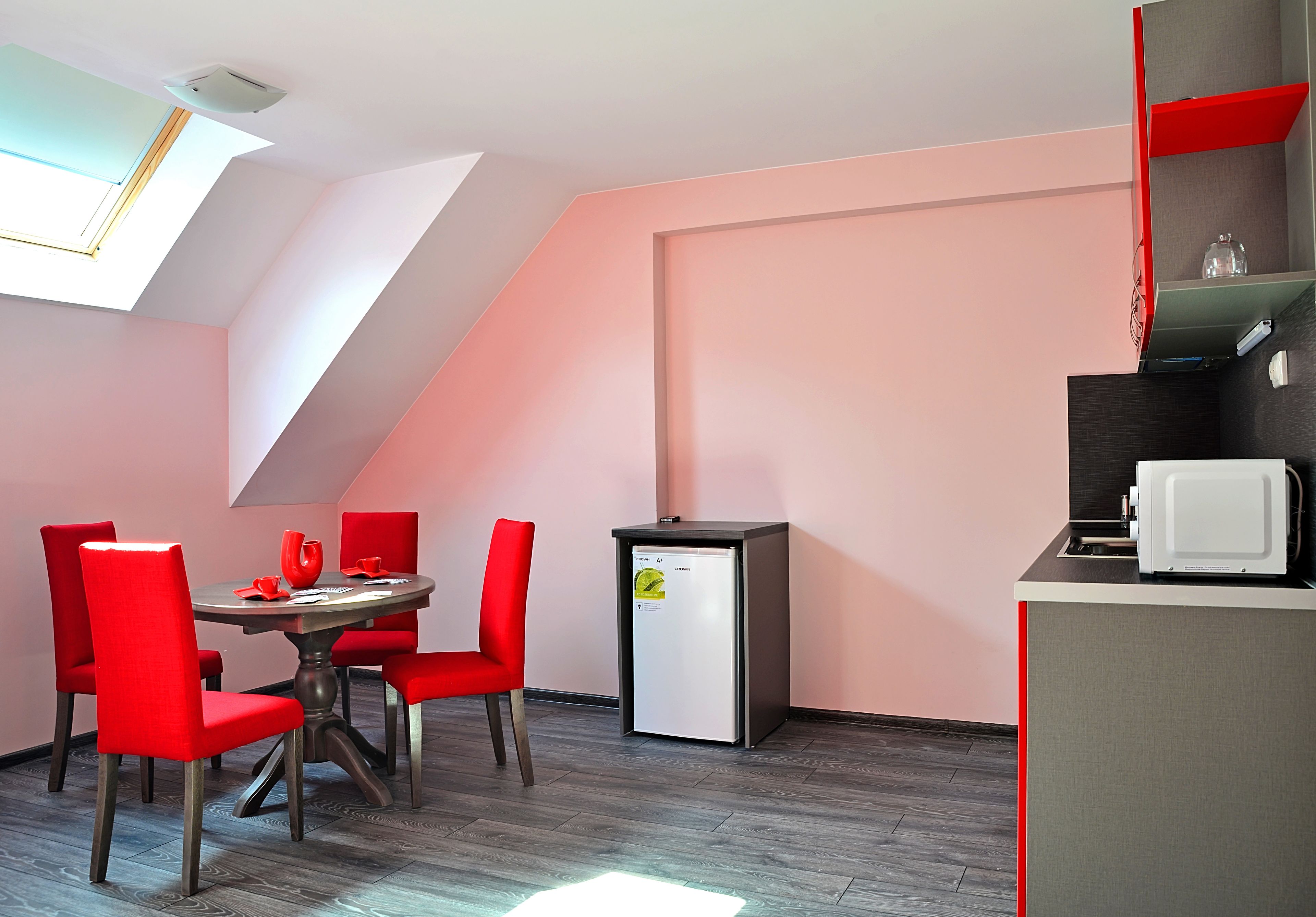 Una habitación compacta con una mesa de comedor y sillas, una pequeña kitchenette y un techo inclinado con tragaluz.
