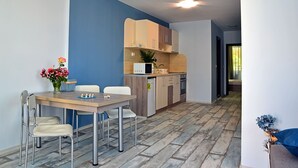 A modern kitchen with a microwave, sink, and cabinets. There is a dining area with a table and chairs, and a vase of flowers. - Visito Apart House (Sofia)