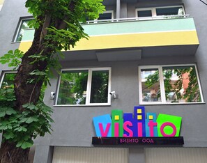 Monikerroksinen rakennus, jossa on värikäs kyltti, jossa lukee ”visito” ja ”ВИЗИТО ООД”. Kyltti viittaa hotelliin tai vastaavaan toimipaikkaan.