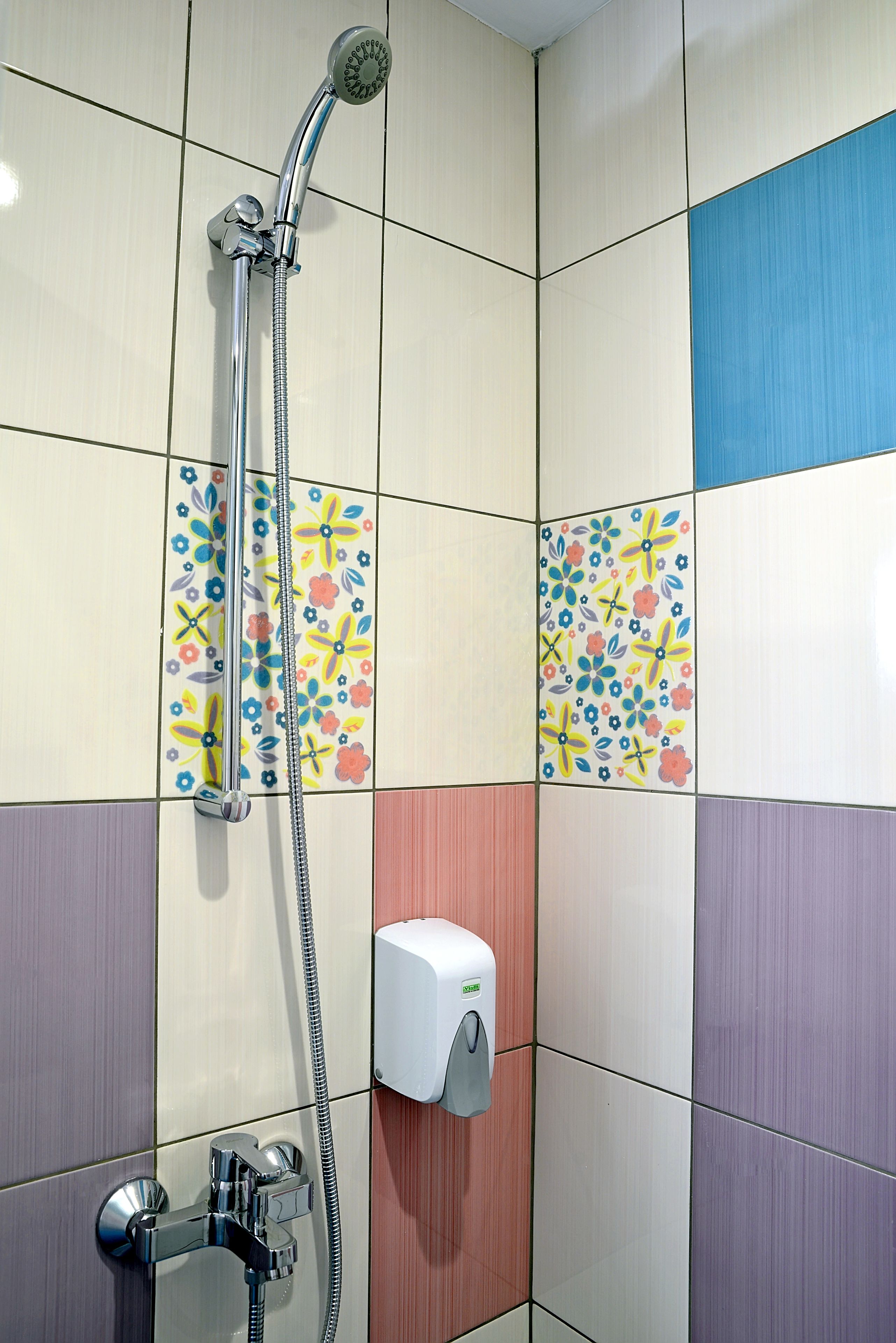 A bathroom with a shower, a soap dispenser, and colorful tiles.
