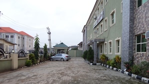 A residential street with a paved driveway, houses with stone and brick facades, and a parked car. - Akma Signature Hotel & Suites (Ibadan)