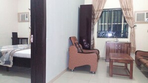 A room with a bed, a wooden chair, a sofa, and a window with curtains. - Akma Signature Hotel & Suites (Ibadan)