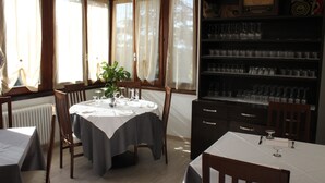 A dining area with a round table set for two, a bookshelf with glassware, and a potted plant. - Albergo Ristorante Bismantova (Castelnovo ne' Monti)