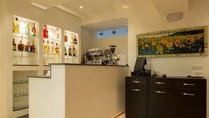 A bar area with a coffee machine, shelves of liquor bottles, and a sunflower painting on the wall. - Albergo Ristorante Bismantova (Castelnovo ne' Monti)