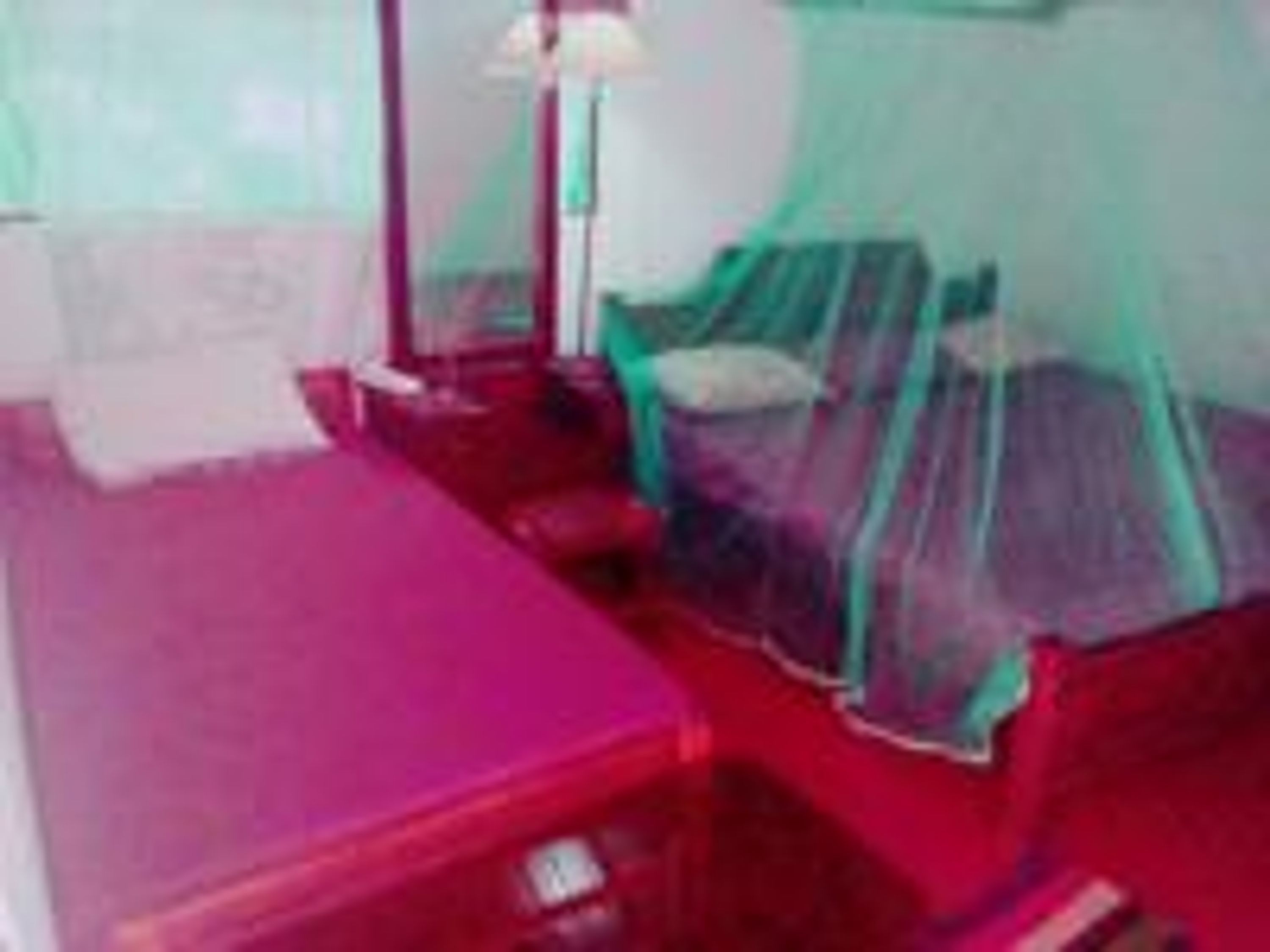A room with a bed covered by a green mosquito net, a bedside table, and a lamp.
