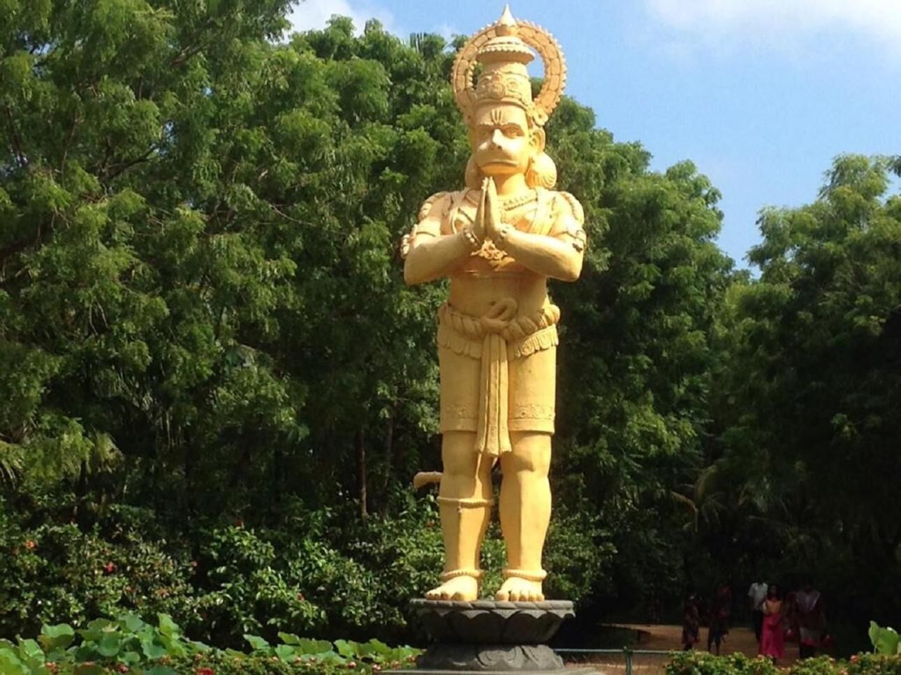 A large golden statue of a deity in a natural setting with lush greenery.