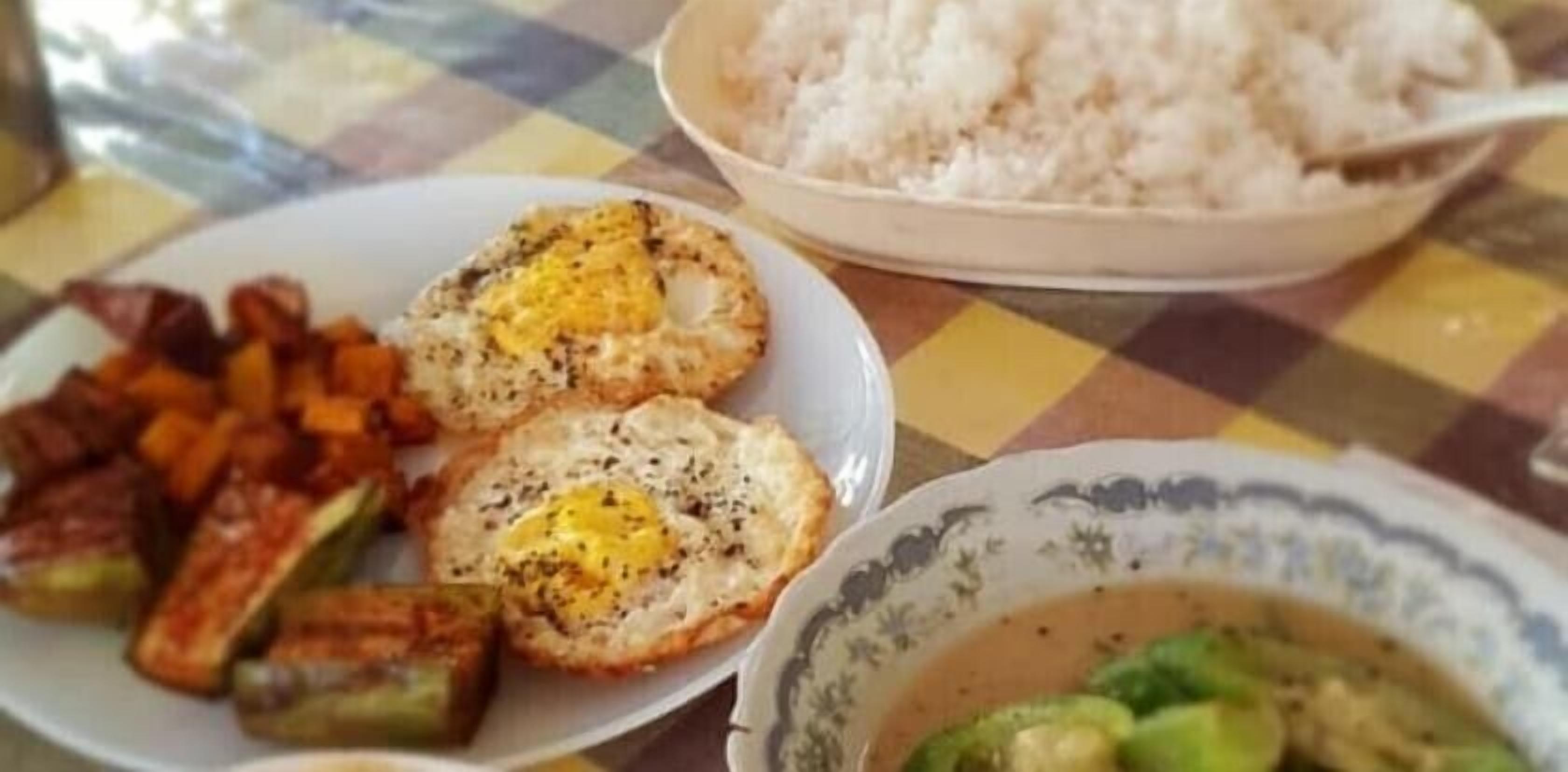 Une table avec une assiette de légumes grillés, deux œufs brouillés, un bol de riz blanc et un bol de soupe.