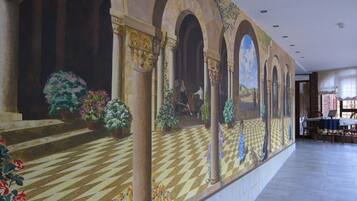 Un couloir doté d’un sol à carreaux, de colonnes et d’une fresque représentant un paysage.