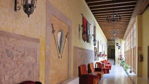 Un vestíbulo de hotel con pared de piedra, asientos rojos y un largo pasillo con ventanas.