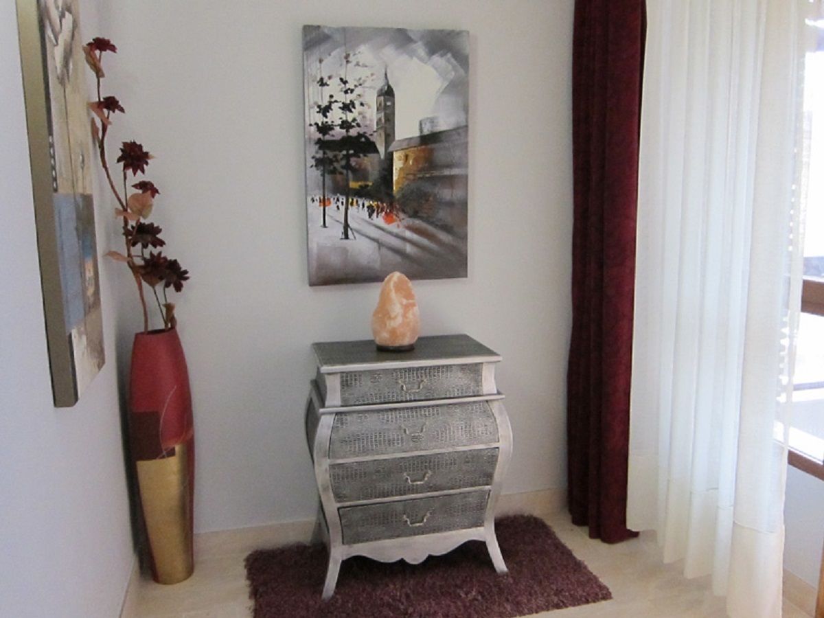A room with a grey dresser, a painting of a cityscape, a vase with flowers, and a red curtain.