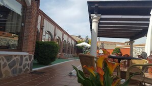 Un patio al aire libre con un edificio de ladrillo, una zona de estar cubierta y un pequeño jardín.