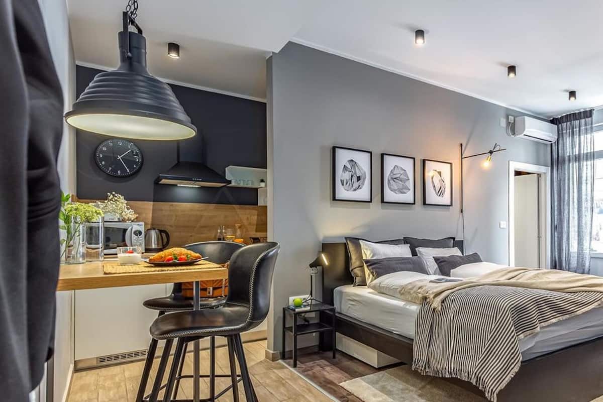 A modern bedroom with a bed, bedside tables, a desk with a chair, a clock, and framed pictures on the wall.