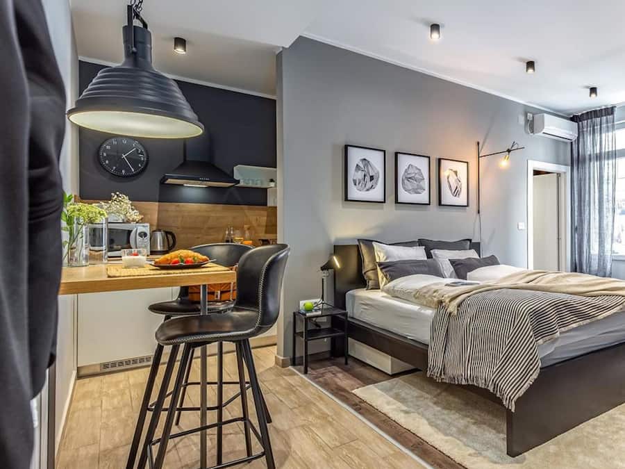 Ein modernes Schlafzimmer mit Bett, Nachttischen, einem Schreibtisch mit Stuhl, einer Uhr und gerahmten Bildern an der Wand.