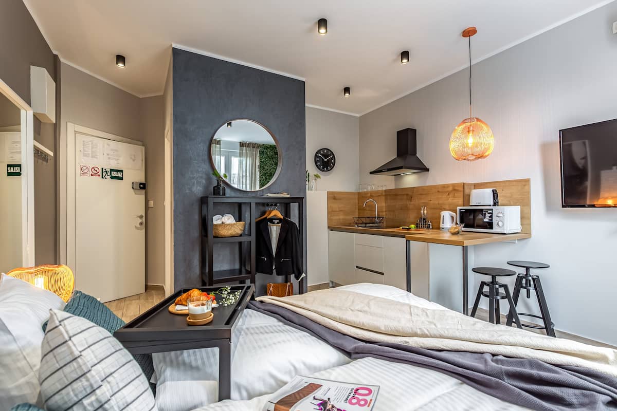 A modern hotel room with a bed, bedside table, and a small kitchenette.