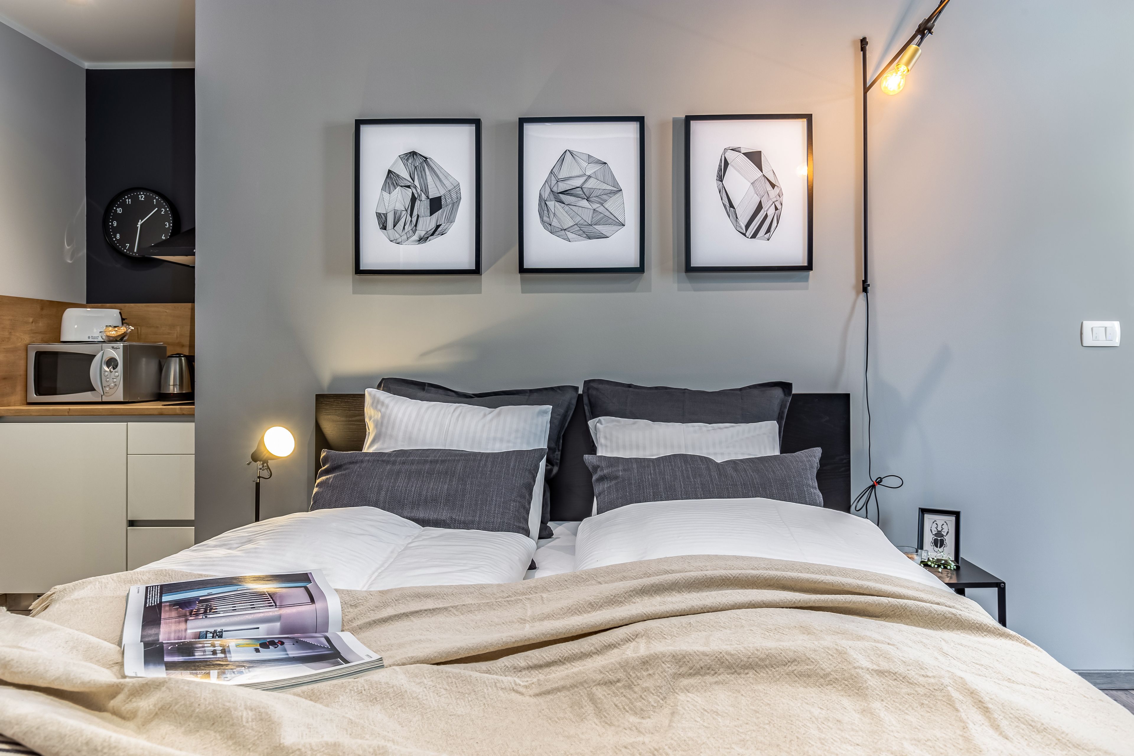 Un dormitorio moderno con una cama, mesitas de noche, un reloj y obras de arte enmarcadas en la pared.