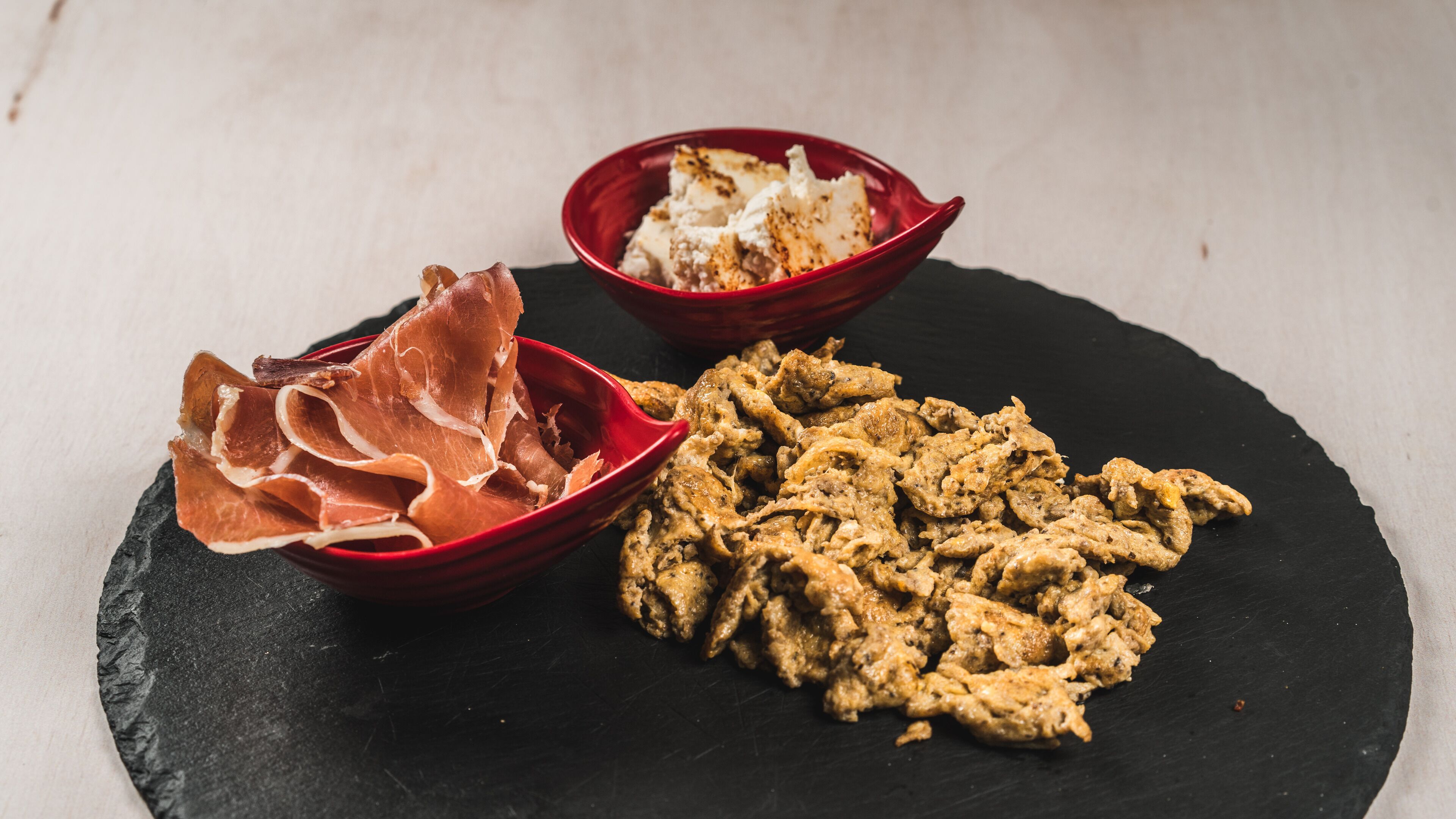 A black slate serving board with three red bowls containing different food items.