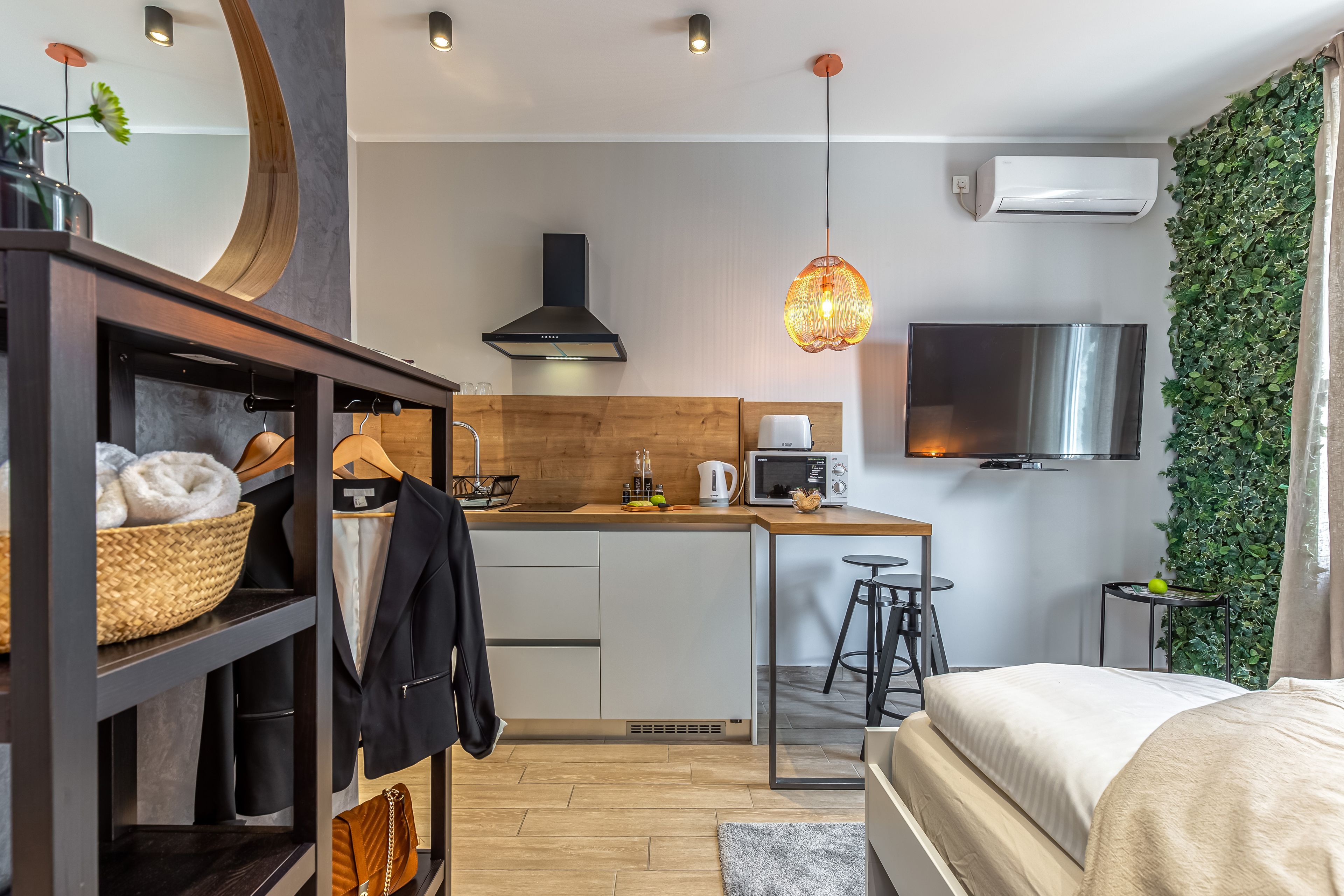 A modern hotel room with a kitchenette, a bed, a wardrobe, and a TV.