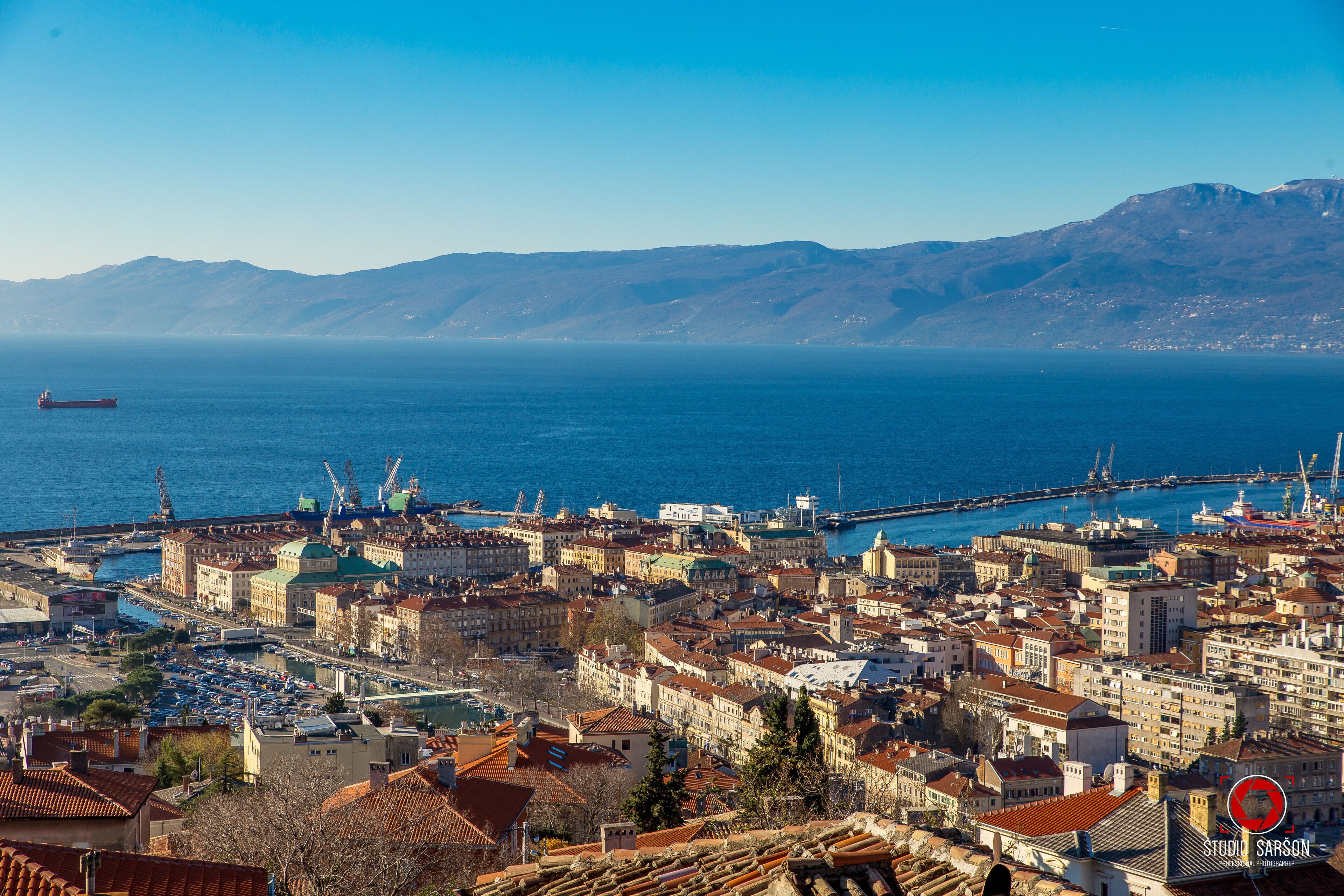 Un paisaje costero con un puerto, edificios y montañas al fondo.