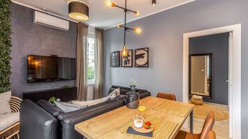 Un salon moderne avec un canapé, une table à manger avec un set de table, un téléviseur et un luminaire suspendu.