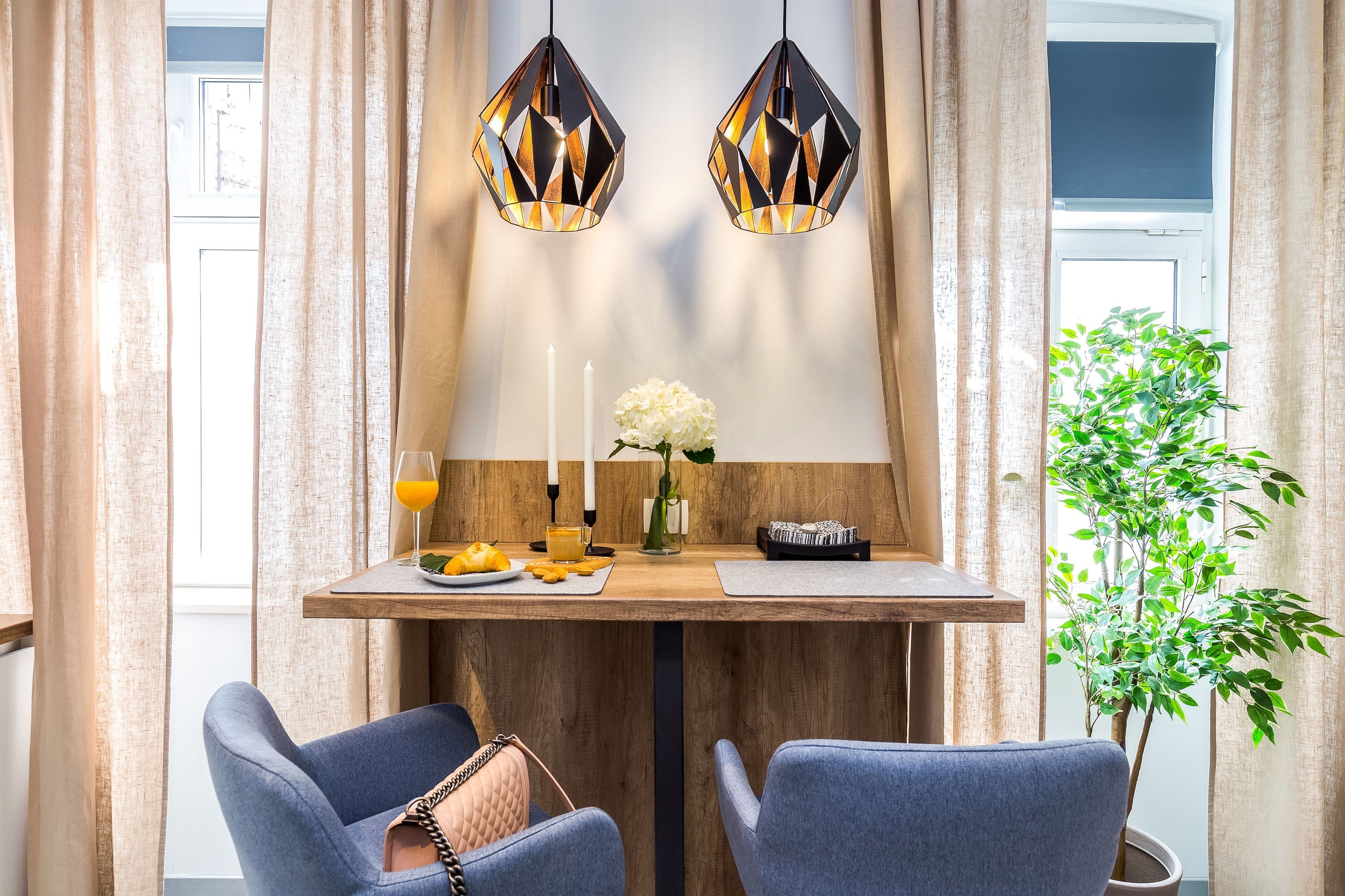 Un comedor con una mesa de madera, dos sillas, un jarrón con flores, velas y una planta.