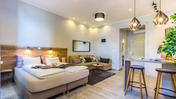 A modern hotel room with a bed, a sofa, a small table, and a bar area.