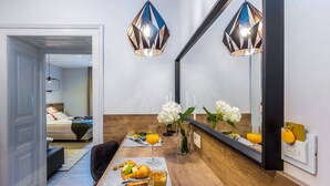 A modern hotel room with a wooden dining table set with breakfast, a mirror, and decorative flowers. - Number 1 Deluxe Apartments (Rijeka)