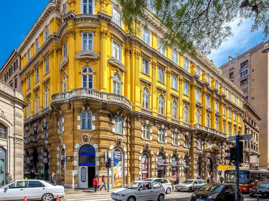 A historic yellow building with multiple storefronts, including a bank and a market.