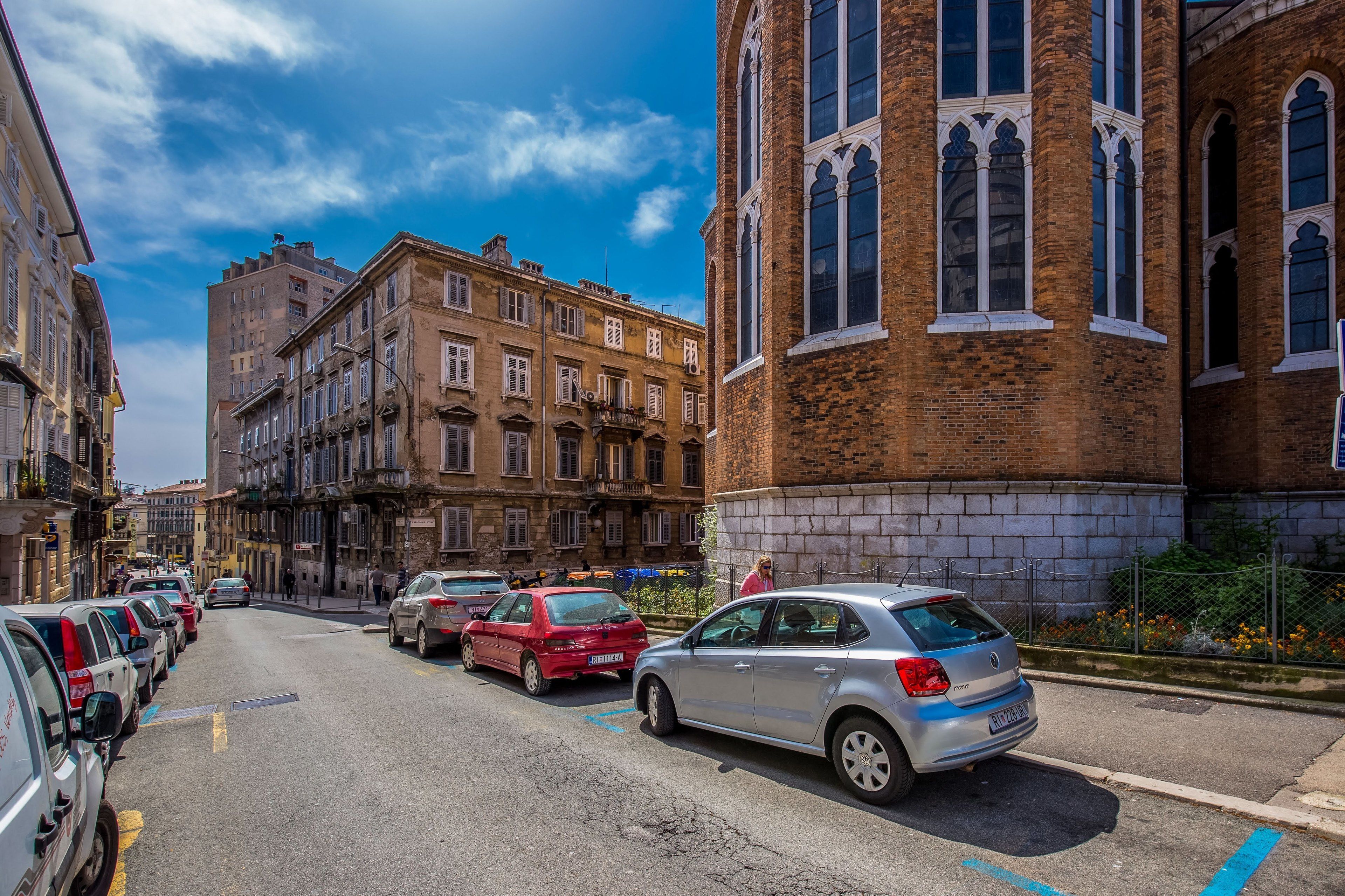 A street with parked cars, historic buildings, and a clear blue sky.