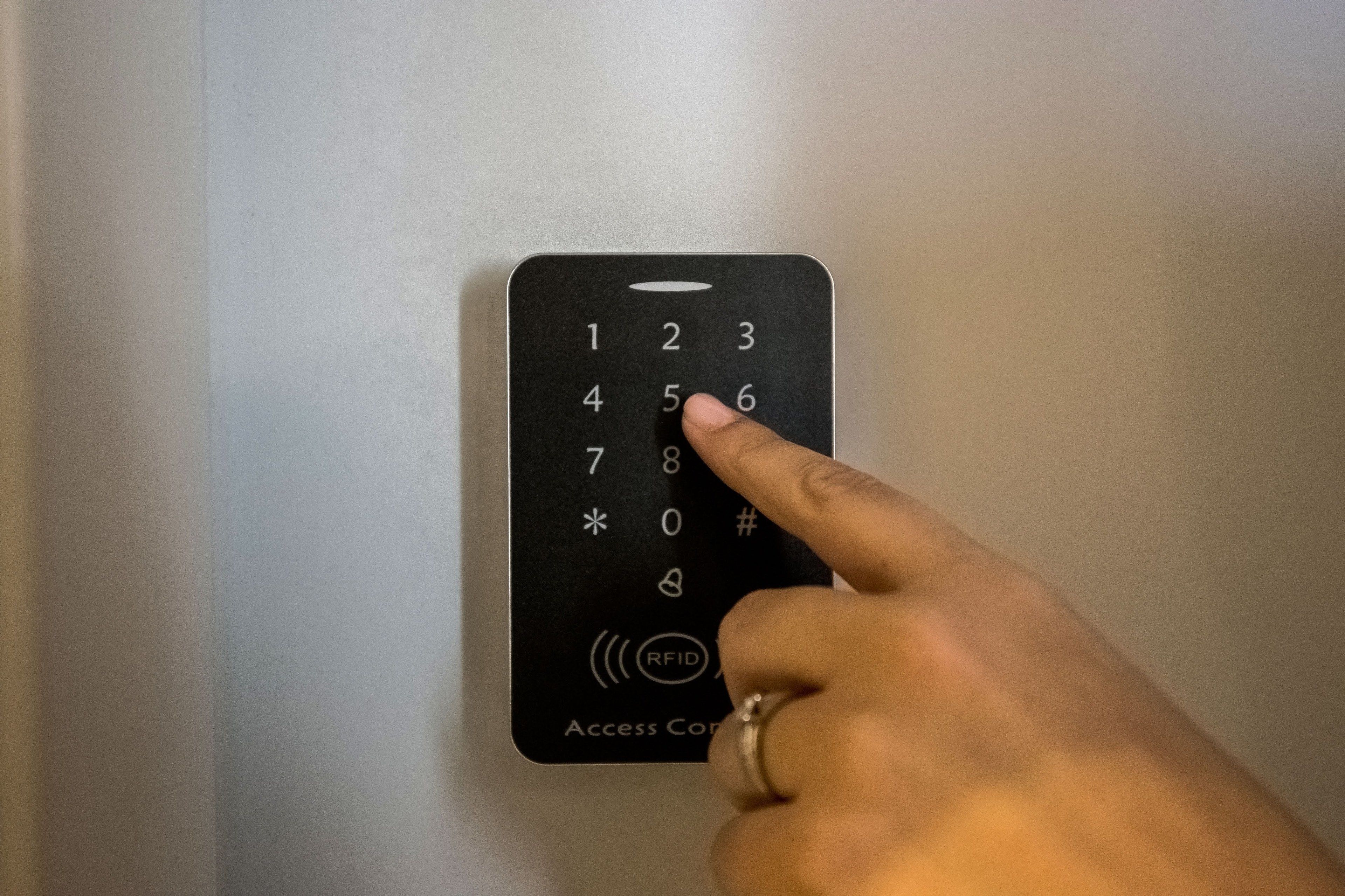 Una mano presionando un botón en un panel de control de acceso negro con teclado numérico y símbolo RFID.
