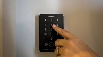 Eine Hand drückt eine Taste auf einem schwarzen Zugangskontrollgerät mit einer Zifferntastatur und RFID-Symbol.