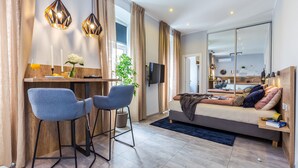 A modern living room with a sofa, two bar stools, a TV, and a dining area with a table and chairs. - Number 1 Deluxe Apartments (Rijeka)