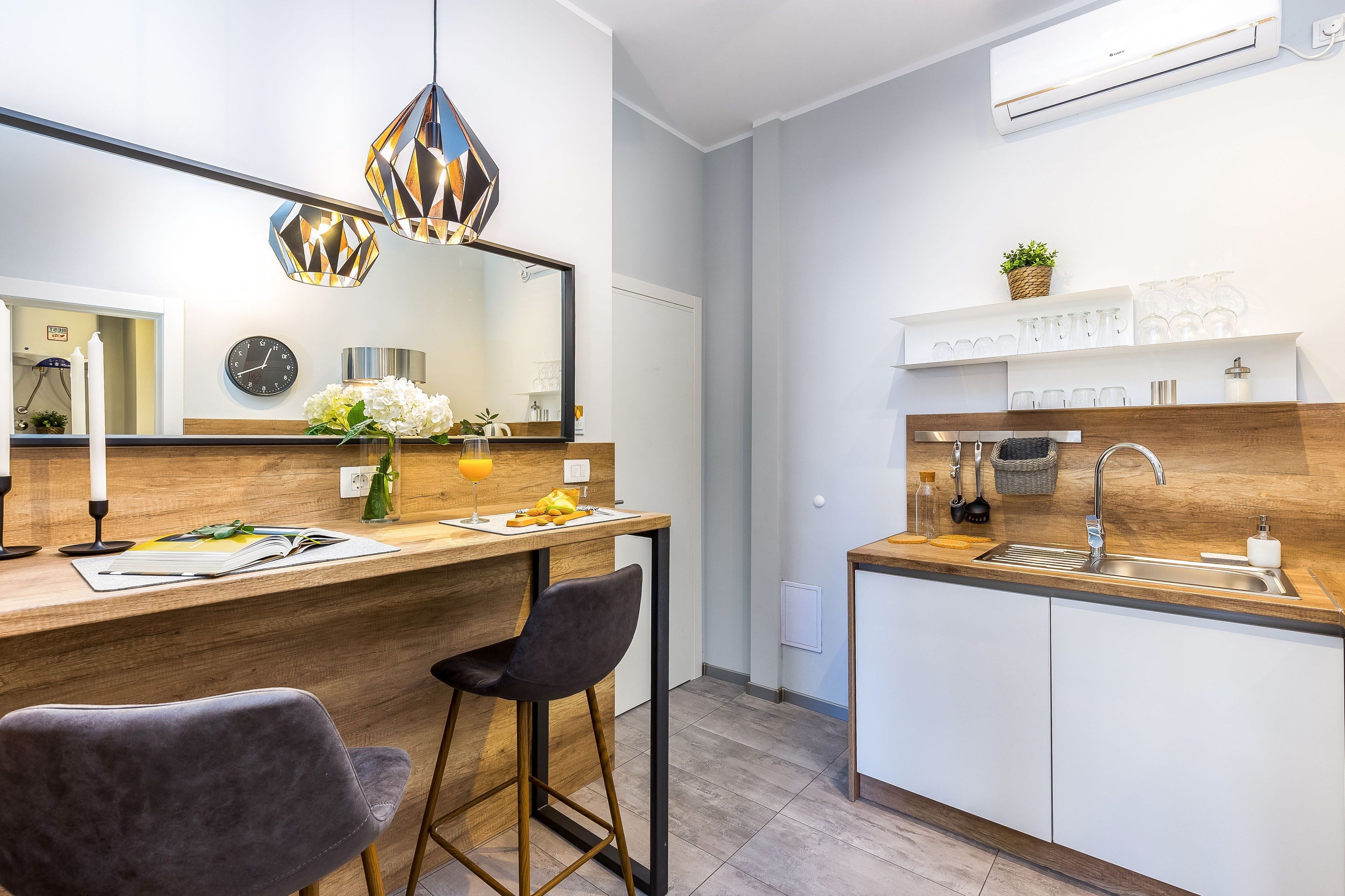 A modern kitchen with a wooden countertop, two bar stools, a hanging light fixture, and a built-in sink.