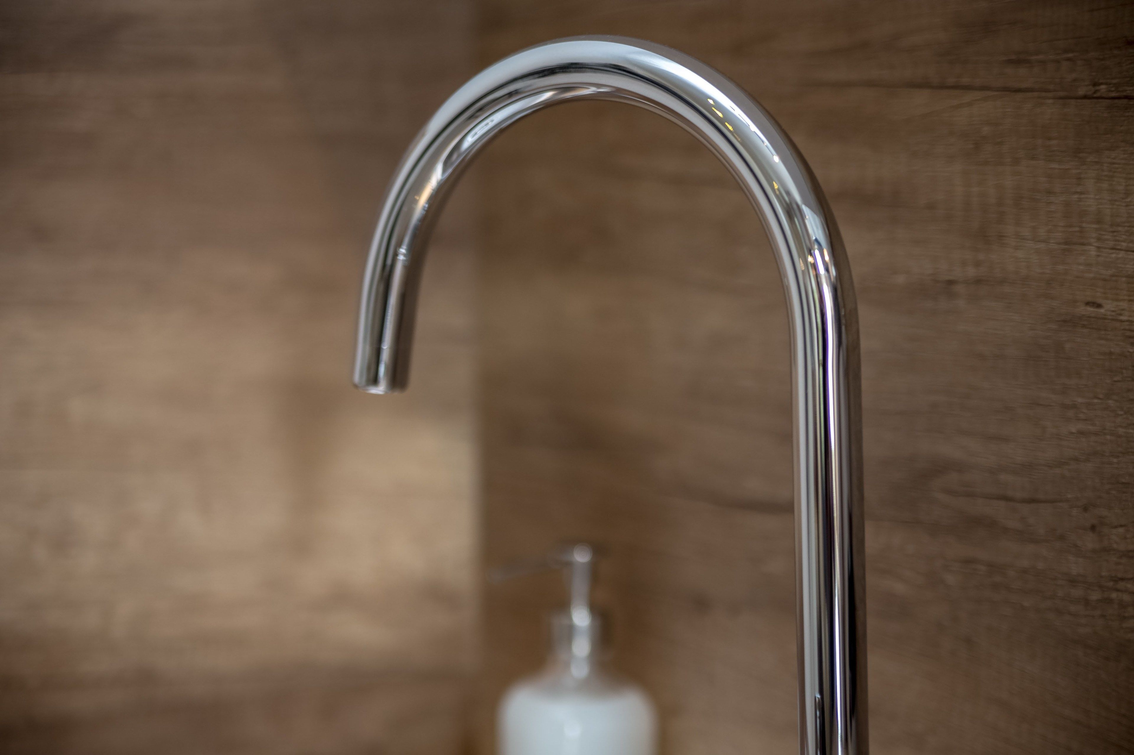 A chrome faucet with a curved design, set against a wooden background.