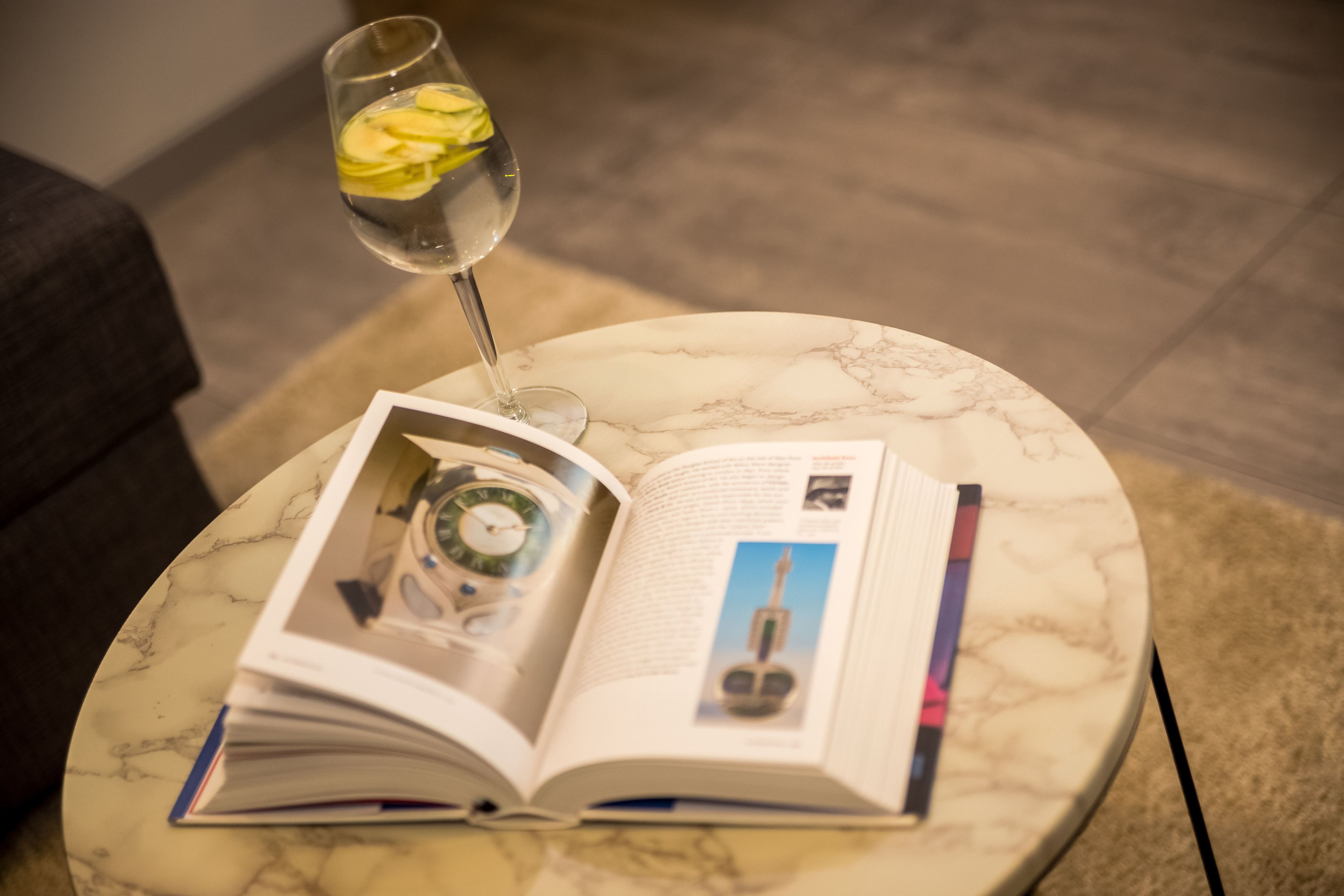 Une table en marbre avec un livre ouvert, un verre d’eau et une horloge.