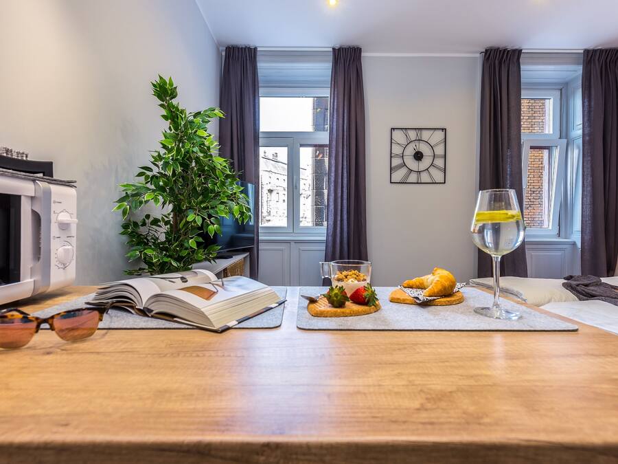 A dining area with a wooden table, a book, a plant, and a glass of wine.