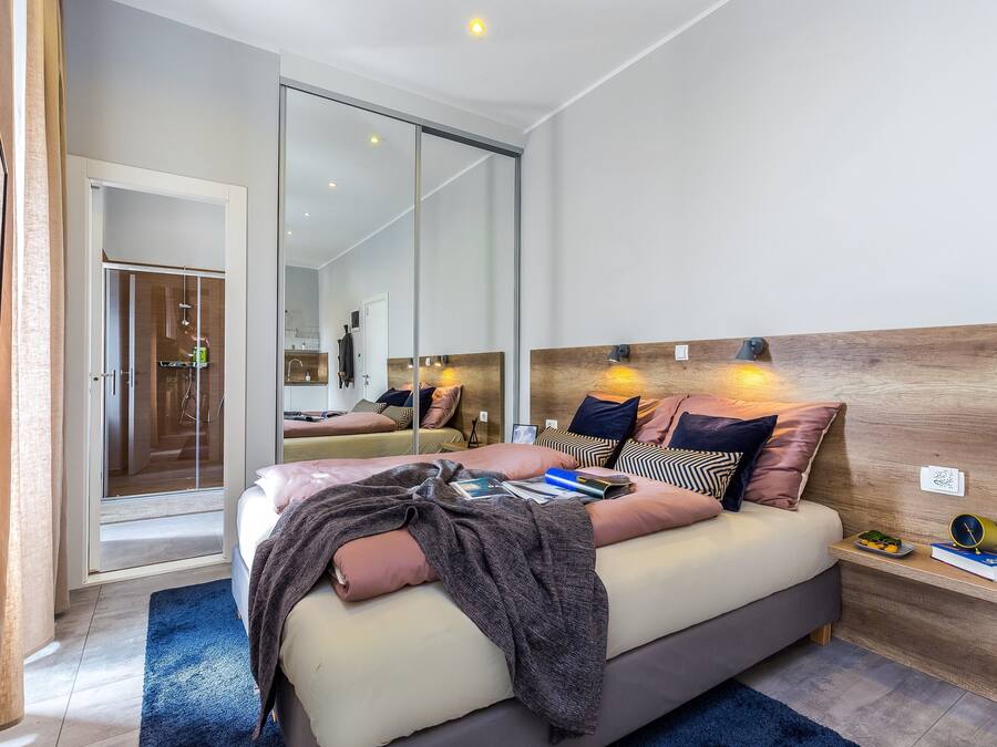 A modern bedroom with a large bed, bedside tables, a mirror, and a sliding glass door leading to a bathroom.