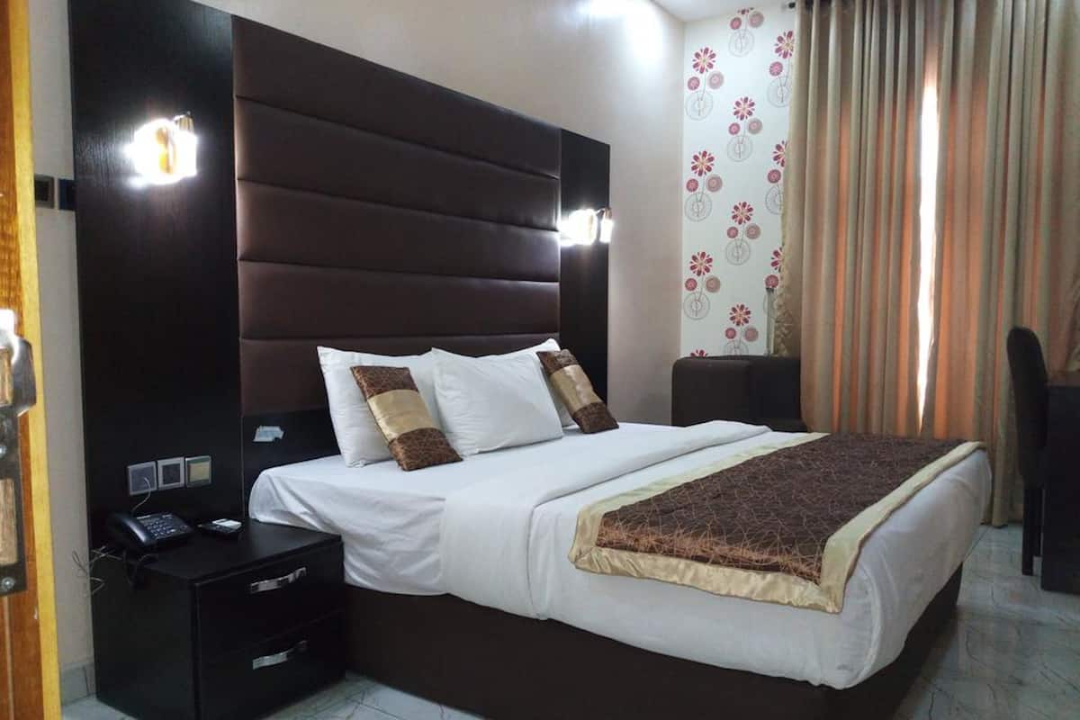 A hotel room with a large bed, a bedside table with a phone, and a nightstand.