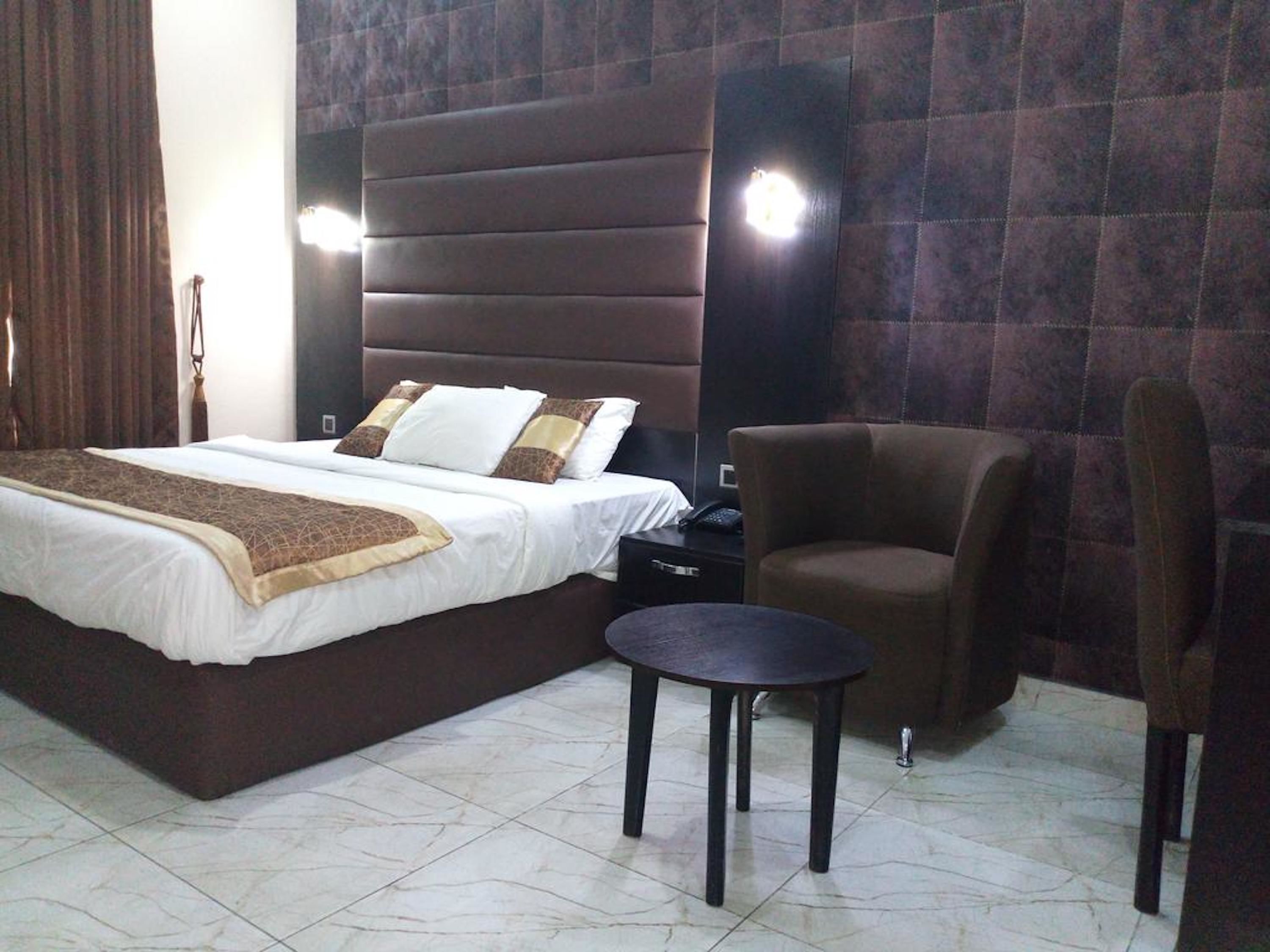 A hotel room with a large bed, a chair, a small table, and a nightstand.