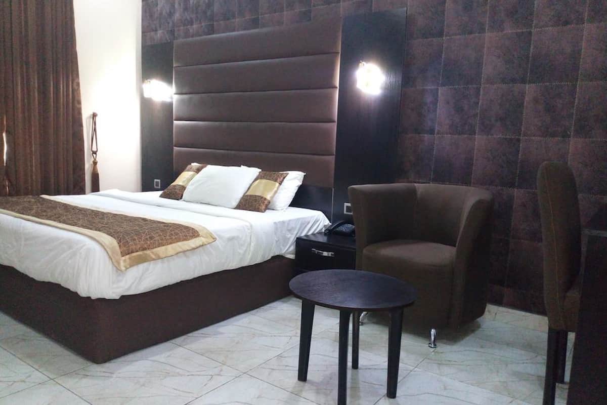 A hotel room with a large bed, a chair, a small table, and a nightstand.