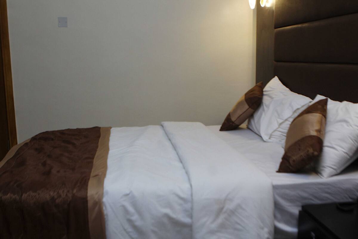A neatly made bed with white and brown bedding, a dark headboard, and a bedside table with a lamp.