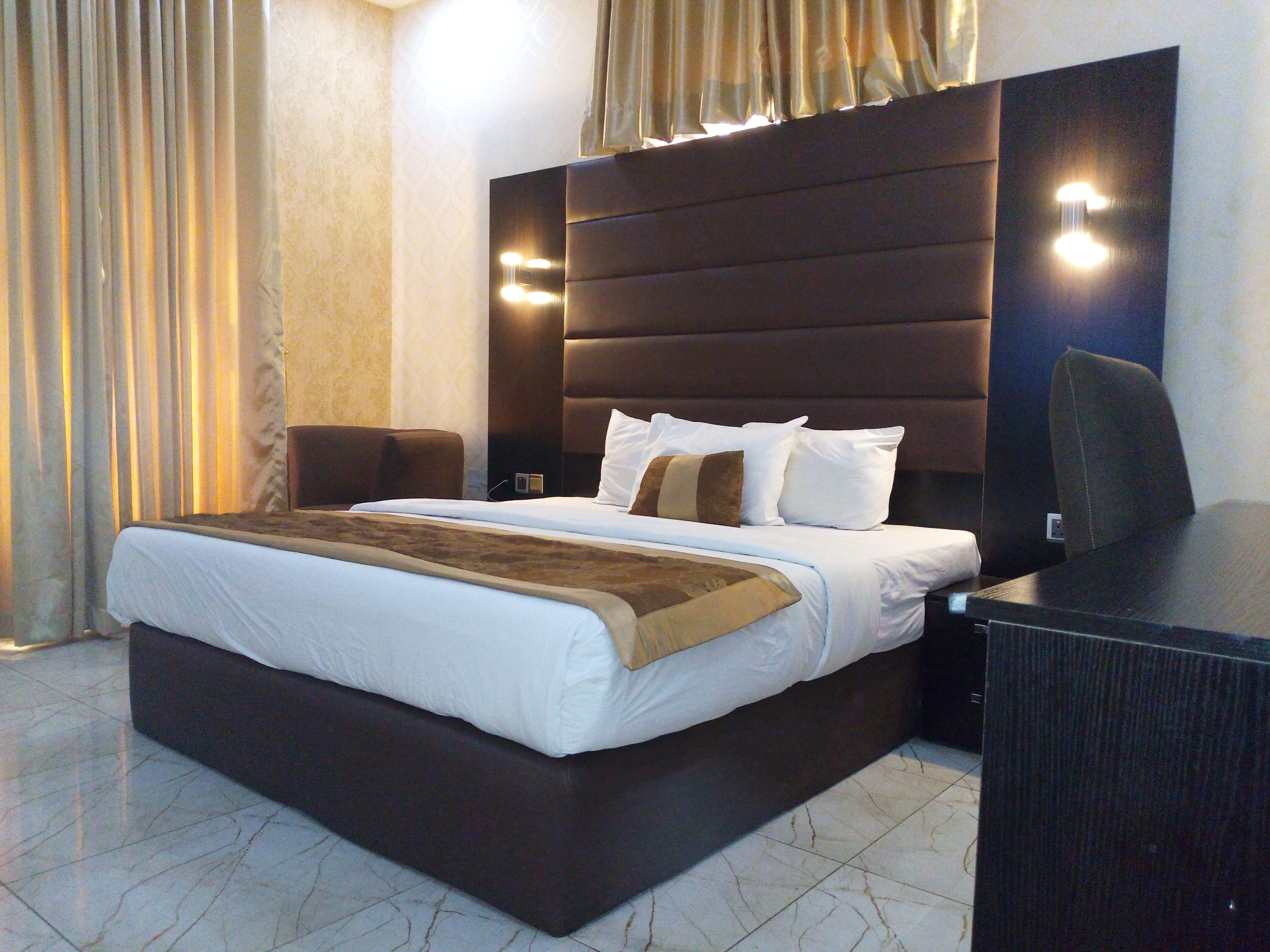 A hotel room with a large bed, a desk, a chair, and a nightstand.