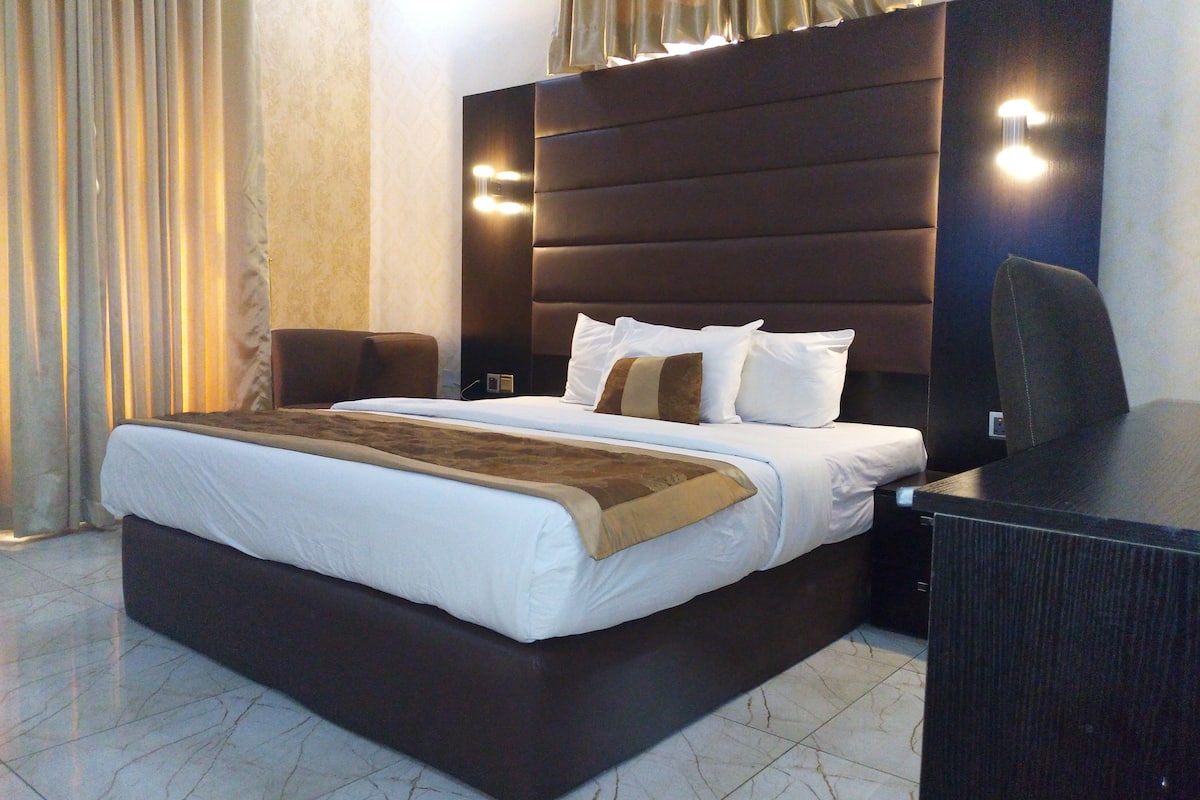 A hotel room with a large bed, a desk, a chair, and a nightstand.