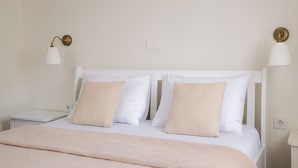 Una cama bien hecha con cabecera blanca y dos almohadas color beige. Hay dos mesitas de noche con lámparas a cada lado de la cama.