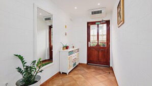 Un pasillo con una planta en maceta, un mueble con azulejos decorativos, una puerta de madera y un cuadro en la pared.