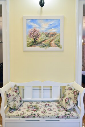 A white bench with floral cushions against a yellow wall, with a framed painting above. - Apartment Tatjana (Zagreb)